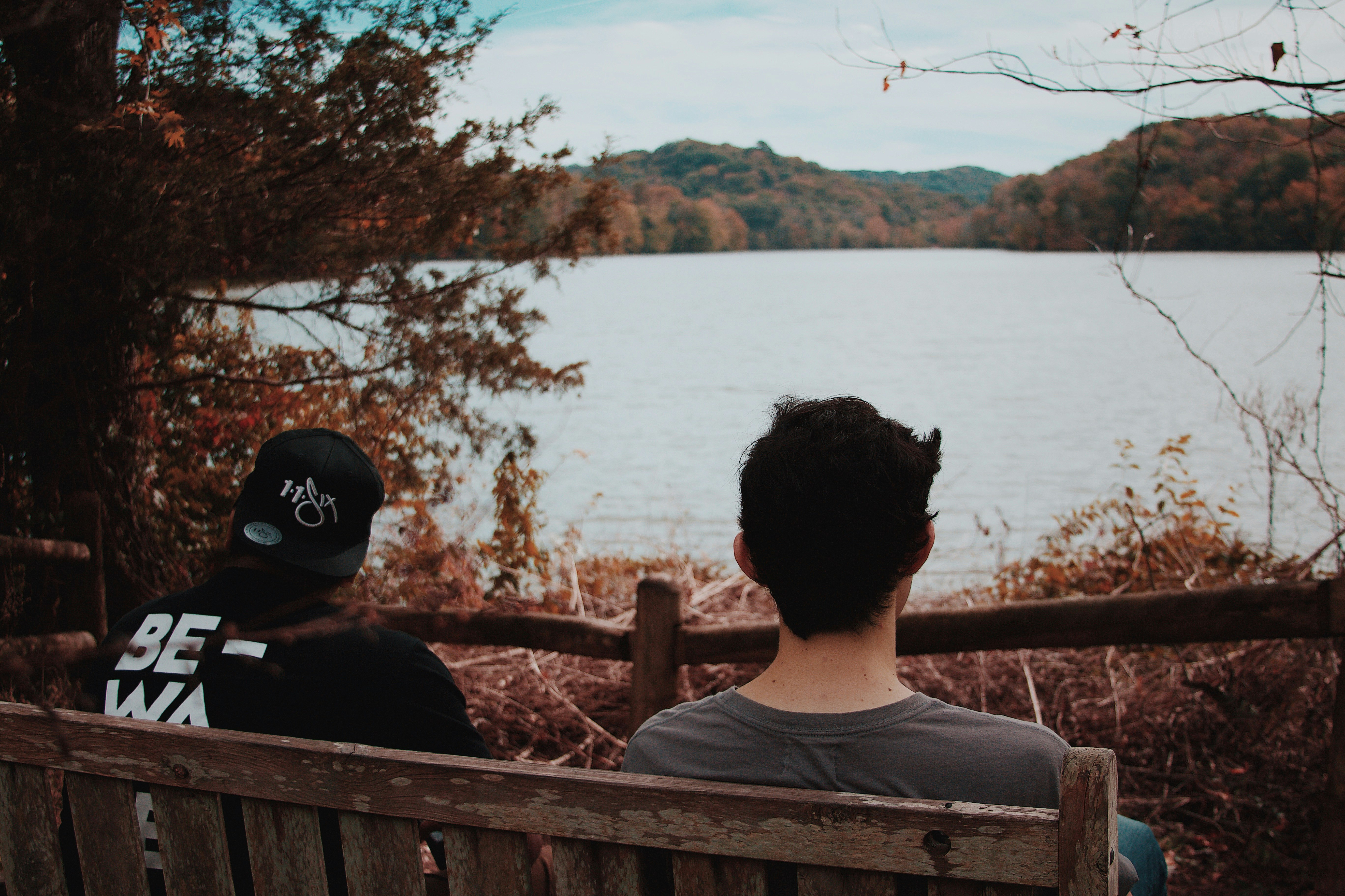 two men sitting on wooden bench looking at body of water